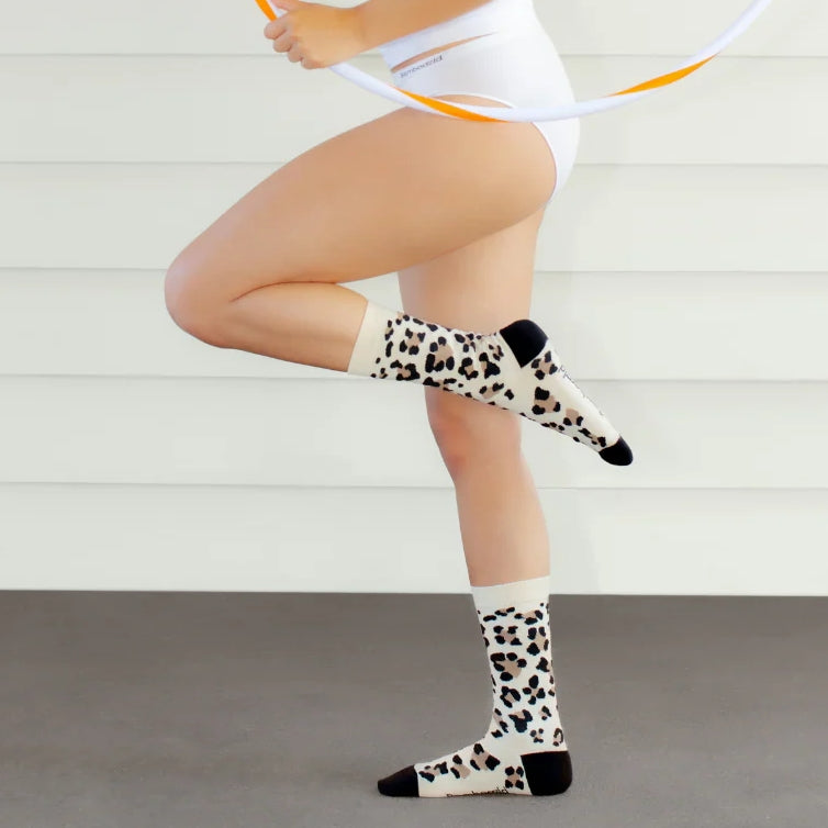 Person wearing white shorts and leopard print socks with black toes on a light background