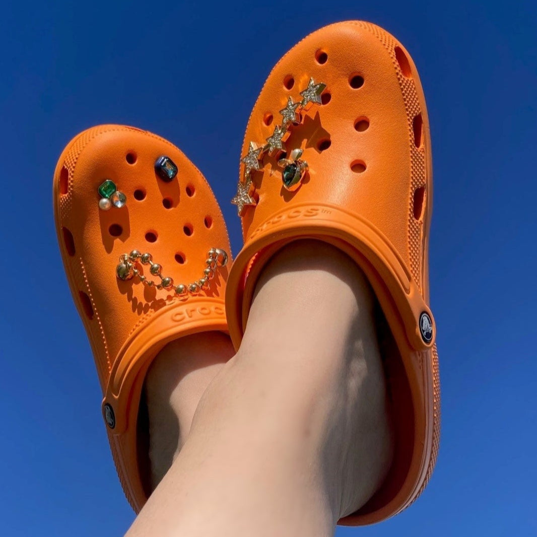 Orange Crocs with decorative elements against a clear blue sky