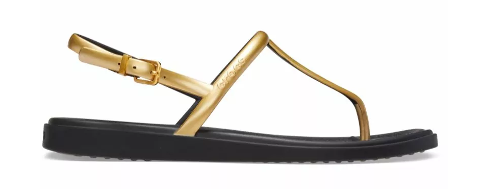 A woman's sandal with metallic gold straps and a black flat sole.