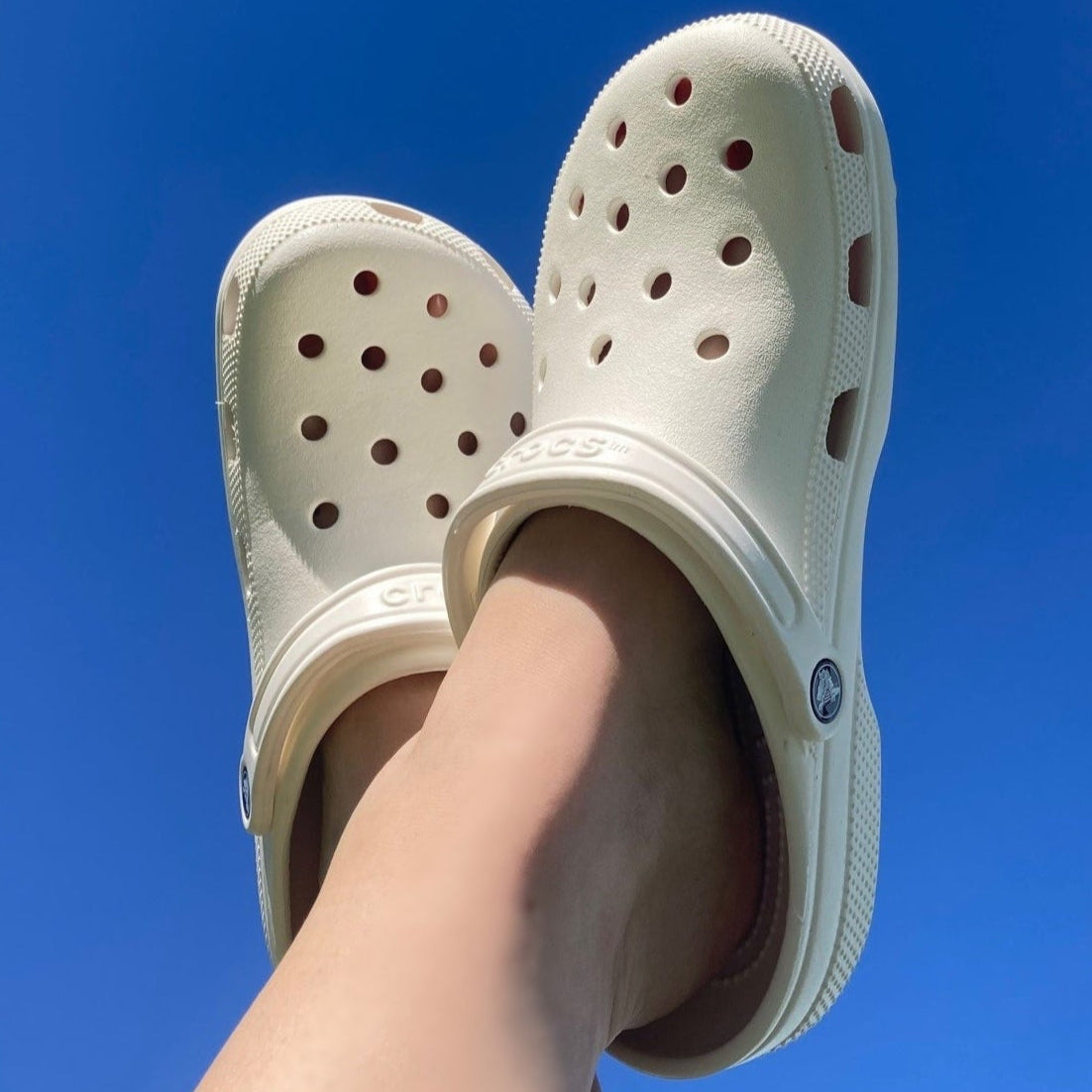 White clogs worn on feet against a clear blue sky